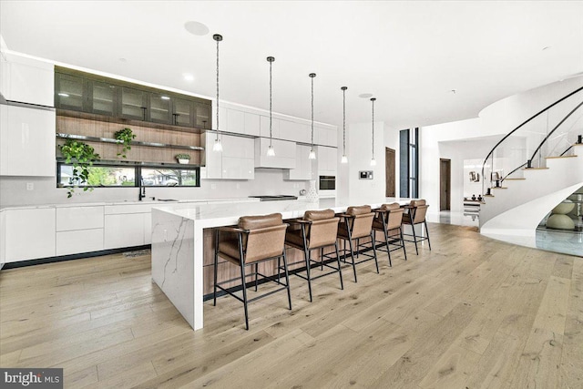 kitchen with modern cabinets, light wood-style flooring, white cabinetry, a sink, and hanging light fixtures