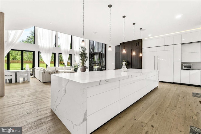 kitchen with modern cabinets, white cabinets, light wood-type flooring, a large island, and light stone counters
