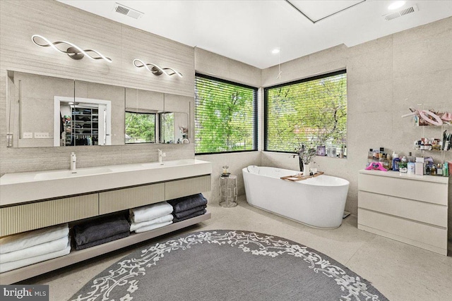 bathroom with a soaking tub, tile walls, and double vanity