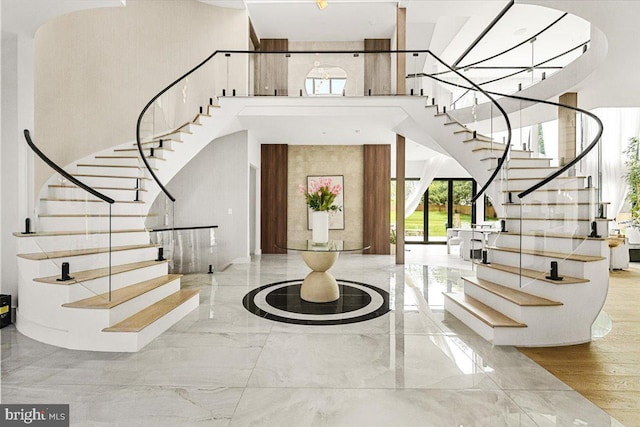 entryway with a towering ceiling, stairs, and marble tiled floors