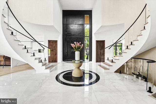foyer entrance with a towering ceiling, marble tiled flooring, and stairway