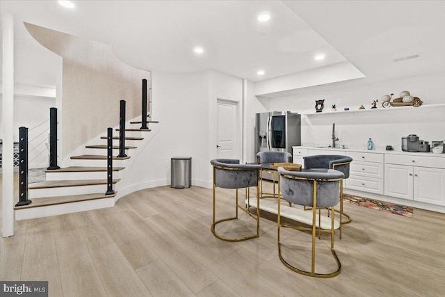 bar area with stainless steel fridge with ice dispenser, a sink, light wood-style flooring, recessed lighting, and baseboards