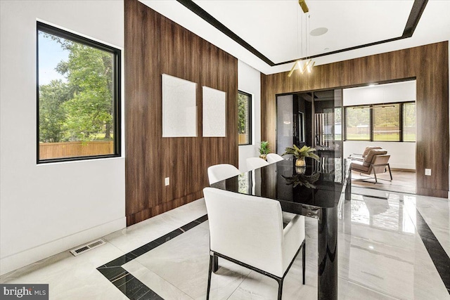 dining space featuring light marble finish flooring, wood walls, inlaid floor details, and baseboards