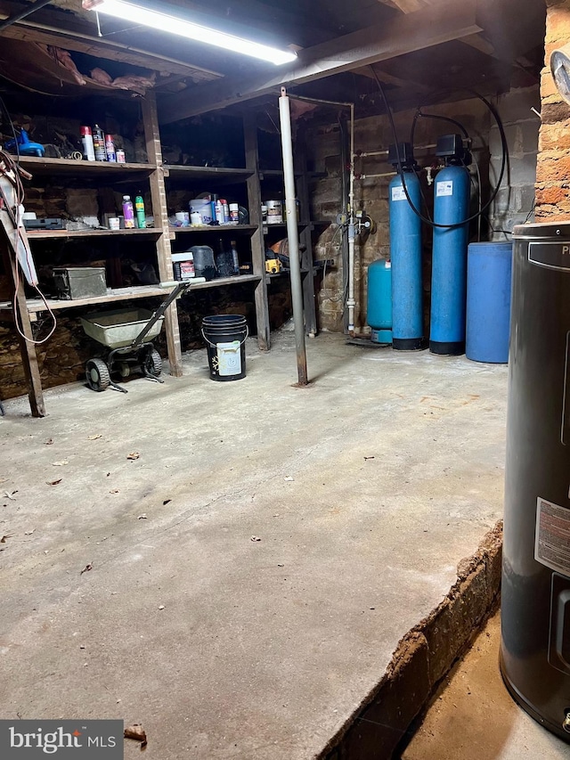 unfinished basement featuring water heater, a water softener system, and a water pressure tank