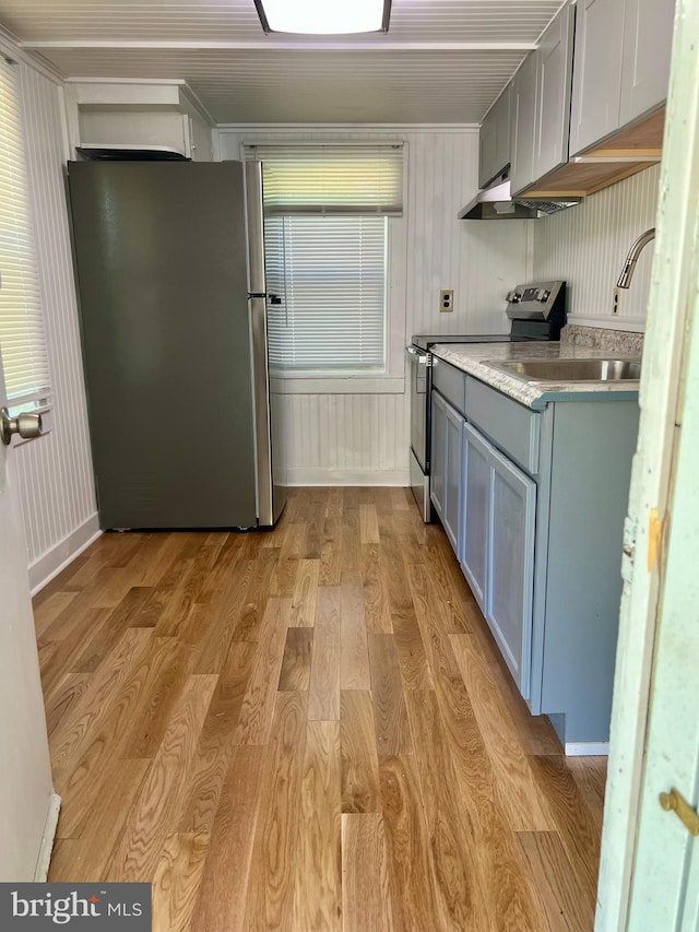 kitchen featuring appliances with stainless steel finishes, light wood-style floors, crown molding, a sink, and light countertops
