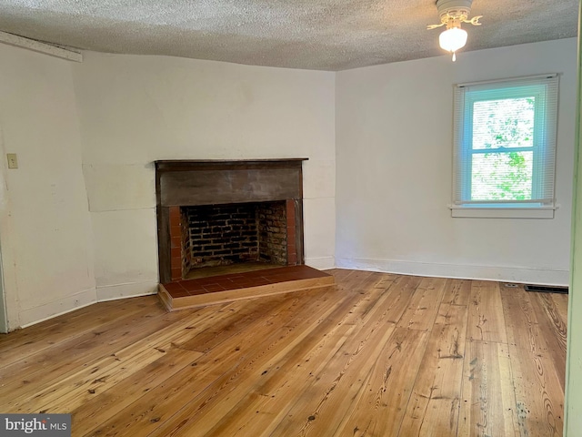 unfurnished living room with hardwood / wood-style floors, a textured ceiling, baseboards, and a fireplace with raised hearth