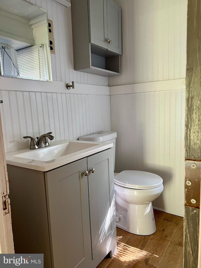 half bathroom featuring wood finished floors, vanity, and toilet