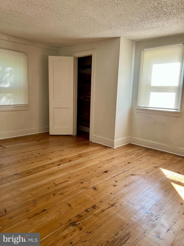 unfurnished bedroom featuring light wood finished floors, a textured ceiling, and baseboards