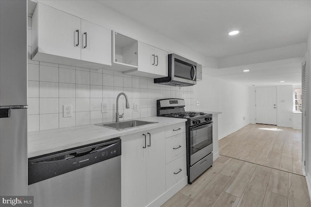 kitchen featuring stainless steel appliances, a sink, white cabinetry, backsplash, and light wood-style floors