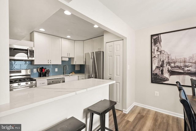 7 Canterbury Sq Unit 401, Alexandria, VA 22304 - kitchen with appliances with stainless steel finishes, baseboards, white cabinetry, a kitchen breakfast bar, and decorative backsplash