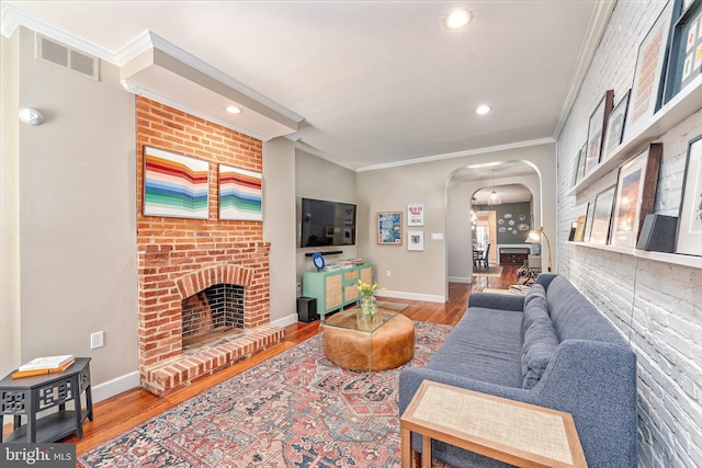 living room with arched walkways, crown molding, a brick fireplace, wood finished floors, and baseboards