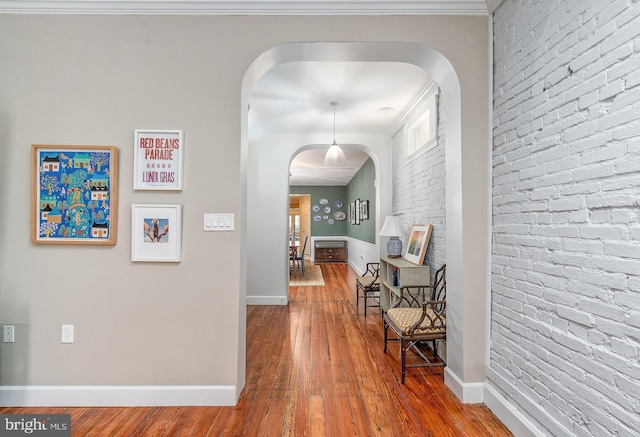 corridor with arched walkways, wood-type flooring, and baseboards