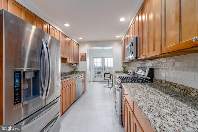 kitchen featuring stainless steel appliances, decorative backsplash, light stone countertops, brown cabinetry, and recessed lighting