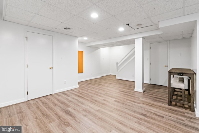finished below grade area with light wood-style flooring, a paneled ceiling, stairway, baseboards, and recessed lighting