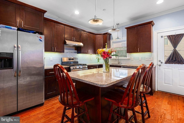 1248 N Hollywood St, Philadelphia, PA 19121 - kitchen featuring appliances with stainless steel finishes, under cabinet range hood, crown molding, pendant lighting, and light wood-type flooring