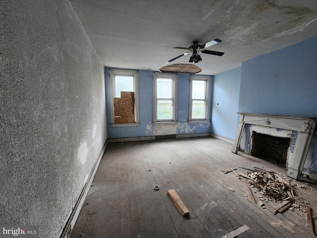 unfurnished living room featuring hardwood / wood-style flooring, a premium fireplace, ceiling fan, and baseboards