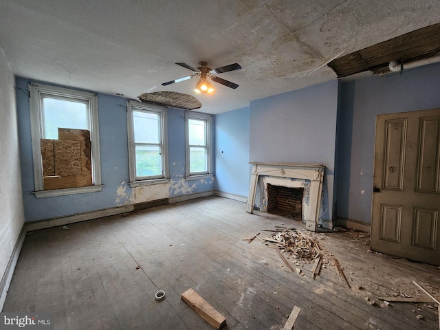 unfurnished living room with a premium fireplace, a ceiling fan, baseboards, hardwood / wood-style flooring, and a textured ceiling