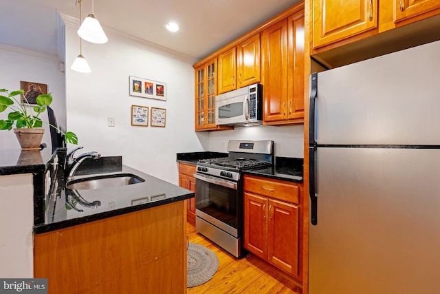 kitchen featuring stainless steel appliances, a sink, ornamental molding, light wood-style floors, and brown cabinetry