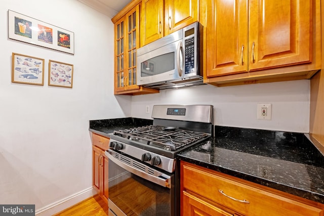 kitchen featuring stainless steel appliances, light wood-style flooring, dark stone countertops, glass insert cabinets, and baseboards