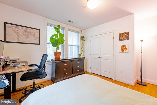 bedroom with light wood-style floors, baseboards, a desk, and a closet
