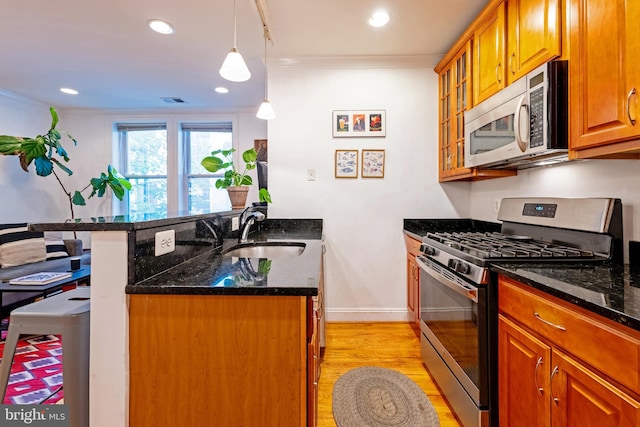 kitchen featuring appliances with stainless steel finishes, a sink, ornamental molding, light wood-type flooring, and dark stone countertops