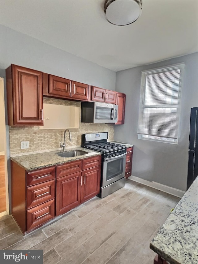 kitchen with stainless steel appliances, a sink, decorative backsplash, light wood-style floors, and light stone countertops