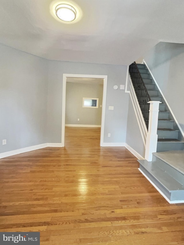 unfurnished living room with wood finished floors, stairs, and baseboards