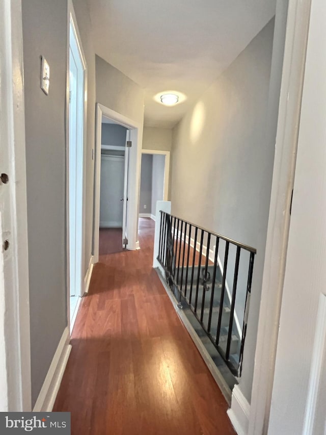 corridor with an upstairs landing, wood finished floors, and baseboards