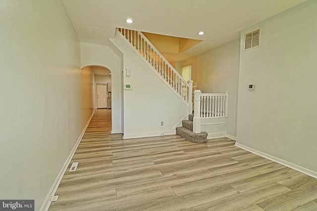 empty room with arched walkways, light wood-style flooring, stairway, baseboards, and recessed lighting