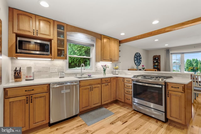 kitchen featuring stainless steel appliances, a peninsula, light wood-style floors, a sink, and light countertops