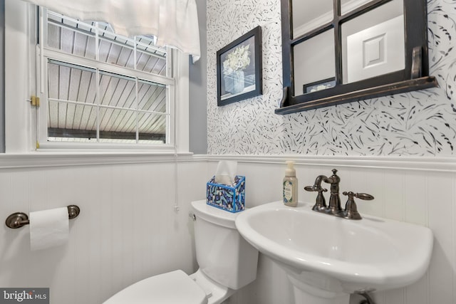bathroom featuring a sink, wainscoting, toilet, and wallpapered walls