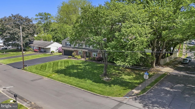 view of property hidden behind natural elements with asphalt driveway, a garage, a front lawn, and brick siding
