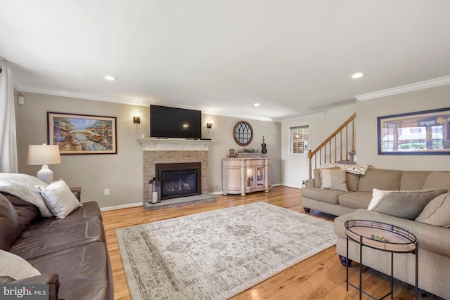 living area with stairway, light wood finished floors, ornamental molding, a glass covered fireplace, and recessed lighting