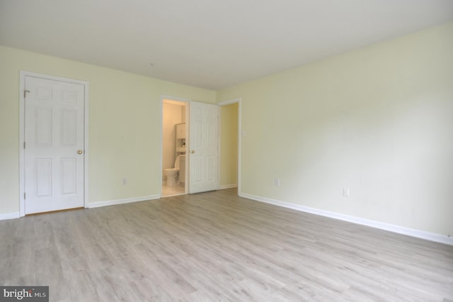 unfurnished bedroom featuring wood finished floors, baseboards, and ensuite bath
