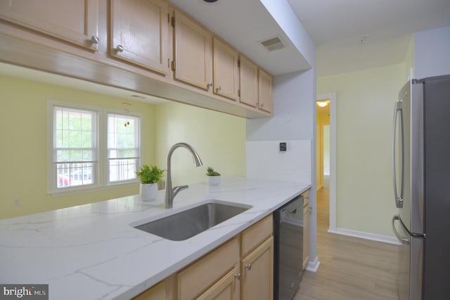 kitchen with freestanding refrigerator, dishwasher, a sink, light wood-type flooring, and light stone countertops