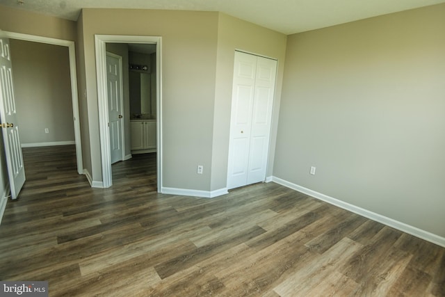 unfurnished bedroom featuring baseboards, dark wood finished floors, and a closet