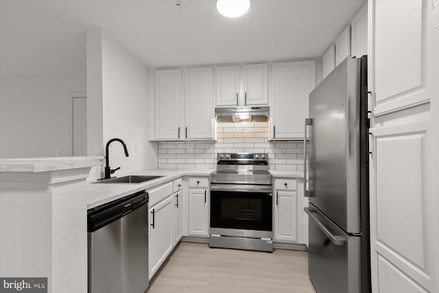 kitchen featuring appliances with stainless steel finishes, a sink, a peninsula, under cabinet range hood, and light countertops