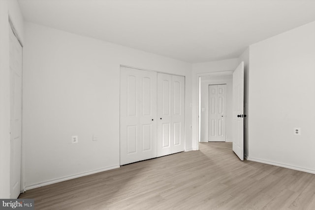 unfurnished bedroom featuring light wood-style floors, baseboards, and a closet