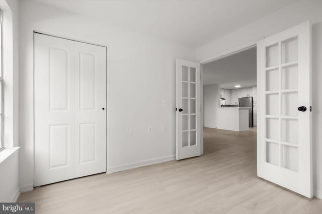 unfurnished bedroom featuring french doors, light wood finished floors, a closet, freestanding refrigerator, and baseboards