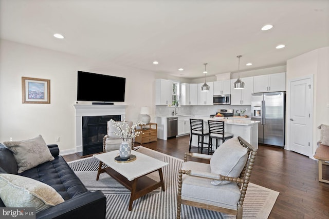 living area with recessed lighting, dark wood-style flooring, a glass covered fireplace, and baseboards