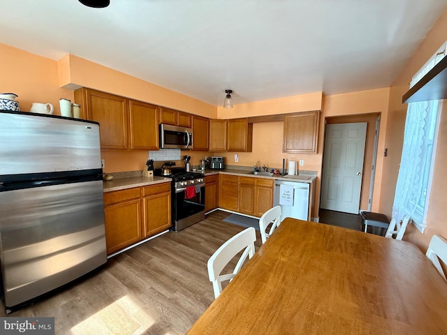 kitchen with stainless steel appliances, dark wood-type flooring, light countertops, brown cabinetry, and a sink