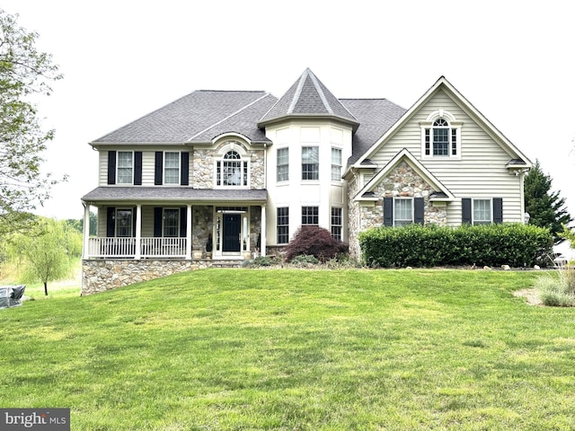 view of front facade with stone siding, a front lawn, a porch, and a shingled roof