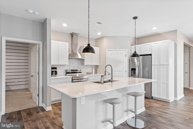 kitchen featuring wall chimney exhaust hood, stainless steel appliances, a sink, dark wood-style flooring, and a kitchen island with sink