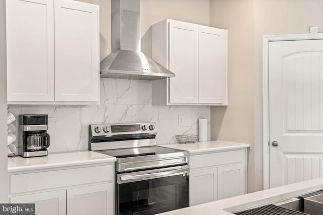 kitchen featuring stainless steel electric range oven, wall chimney exhaust hood, tasteful backsplash, and white cabinets
