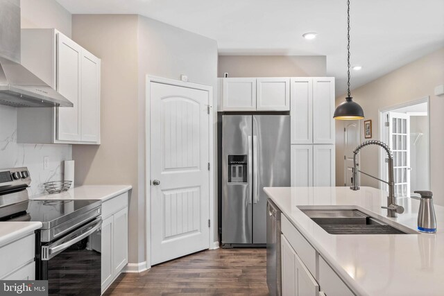 kitchen with appliances with stainless steel finishes, wall chimney exhaust hood, a sink, dark wood finished floors, and white cabinets