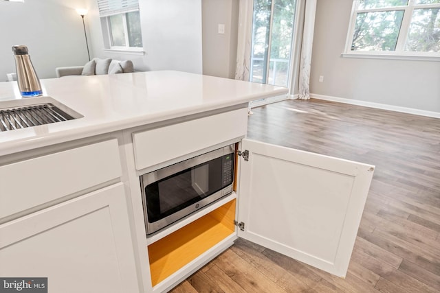 kitchen featuring stainless steel microwave, light wood-type flooring, white cabinets, light countertops, and baseboards