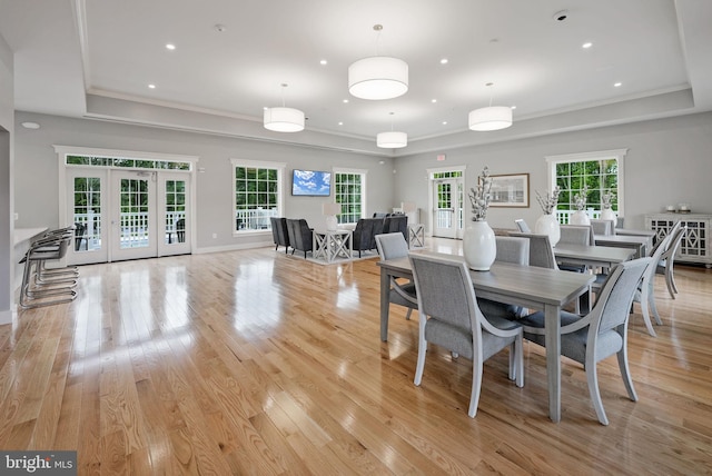 dining space featuring a raised ceiling, light wood-style floors, recessed lighting, ornamental molding, and french doors