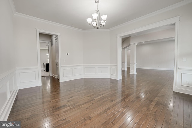 empty room featuring dark wood-style flooring, crown molding, a chandelier, decorative columns, and a decorative wall