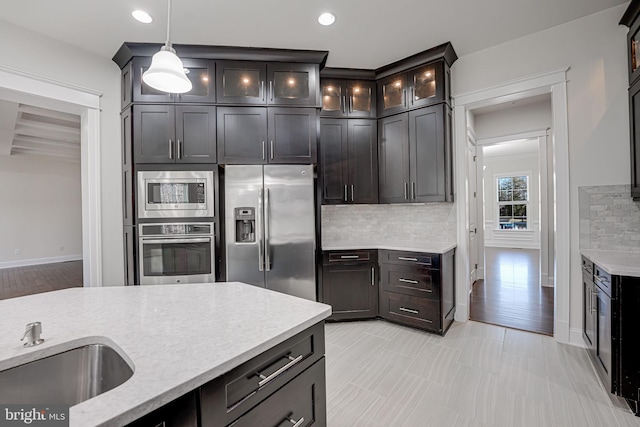 kitchen with stainless steel appliances, a sink, backsplash, decorative light fixtures, and glass insert cabinets