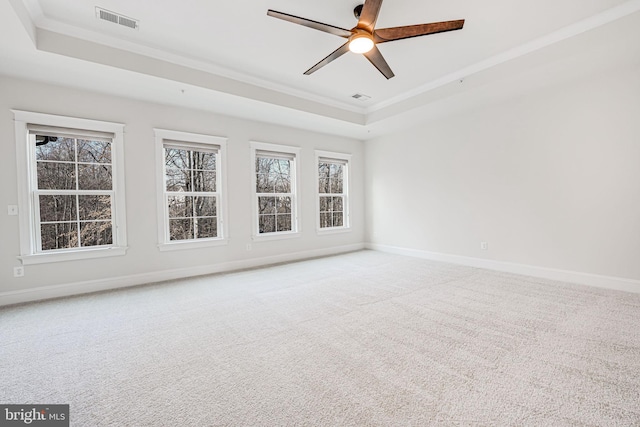 empty room with a tray ceiling, crown molding, carpet flooring, and baseboards